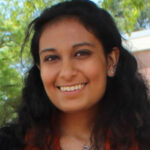 Headshot of Oneeka Kohli wearing a black dress and orange stole.