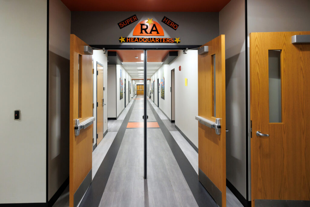 The entrance to a hallway  features a sign that says "RA Super Hero Headquarters" above open double doors.