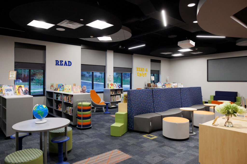 A modern school media center features books in low bookshelves, couches, tables and chairs.