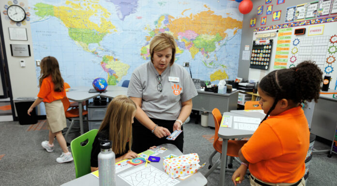 Finding their superpowers: Mercer launches Roberts Academy for dyslexic children A elementary-aged student sits at a desk in a modern classroom while listening to the teacher who is standing next to the child and pointing to a card in her hand. Other students are seen in the picture, and a world map fills the back wall.