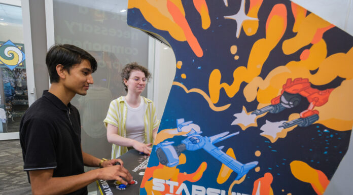 Mercer students design, develop space-themed arcade game Mercer University students Rajwol Chapagain and Maret McWhorter play an arcade video game. The side of the arcade cabinet show a blue and red space ship battling each other in outer space against a blue background with yellow and orange accents. The words "Starship Showdown" are visible.