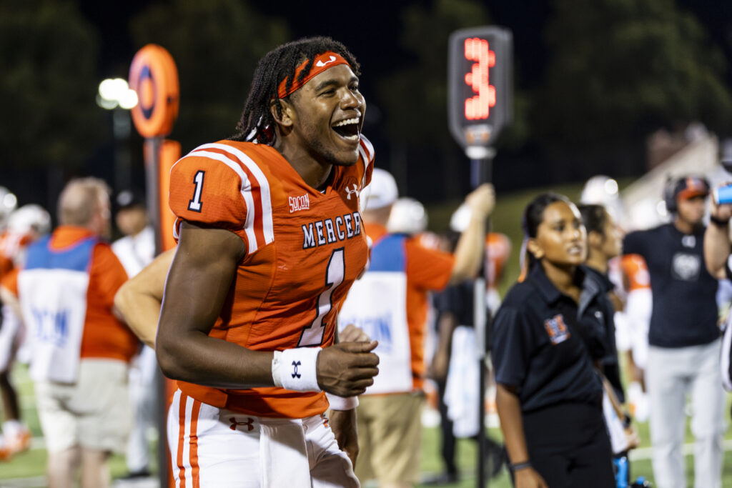 A football player wearing a Mercer uniform smiles with glee and pumps his arm.