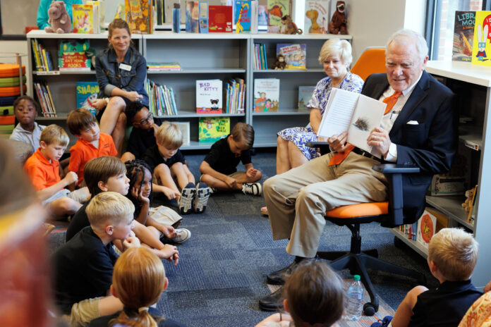 Former Georgia Gov. Nathan Deal, wearing an orange tie and navy blue blazer, shows a picture in a book to a group of attentive children inside a library.