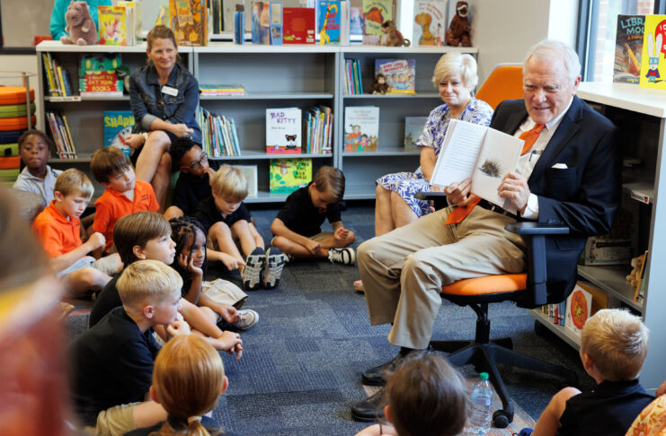 Former Georgia Gov. Nathan Deal, wearing an orange tie and navy blue blazer, shows a picture in a book to a group of attentive children inside a library.