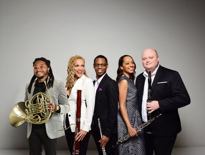 Five musicians pose with wind instruments