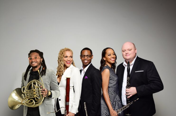 Five musicians pose with wind instruments