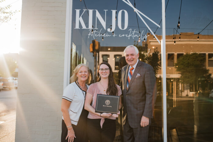 Dr. Penny Elkins, Chelsea Hughes and William D. Underwood standing in front of "Kinjo Kitchen + Cocktails" restaurant, smiling as Chelsea holds her diploma.