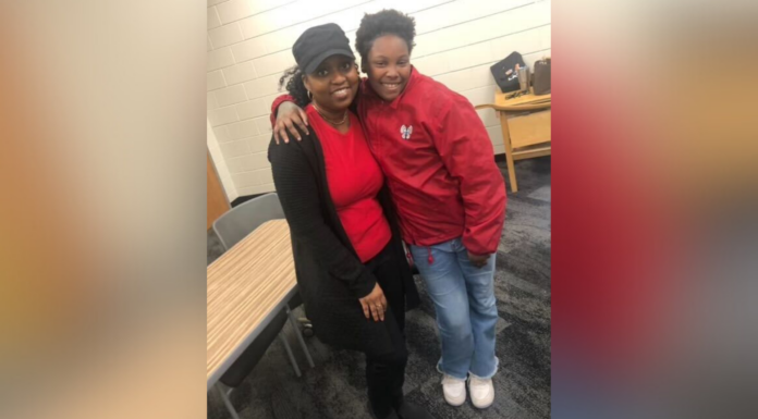Mercer Law staff member supports, inspires teen girls through mentorship program Two individuals in red tops and black pants, one wearing a cap, smiling and embracing in a room with tables and chairs in the background.