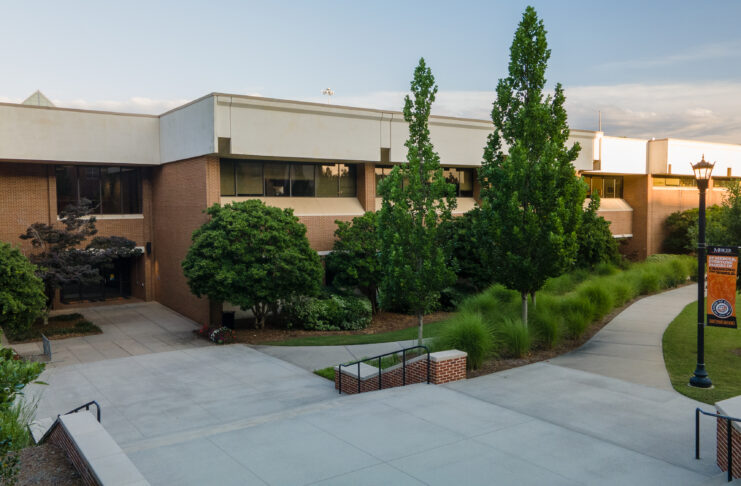 Exterior of the School of Medicine, a two story brick building with a flat room and landscaping.