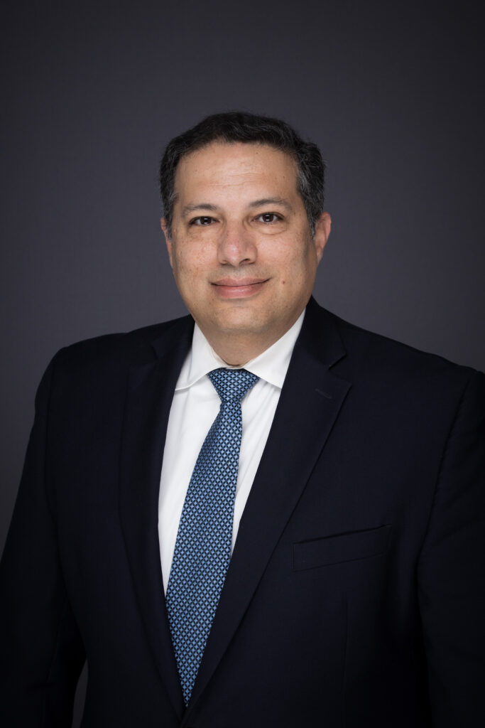 A headshot of a man wearing a blue tie, white dress shirt and black blazer.