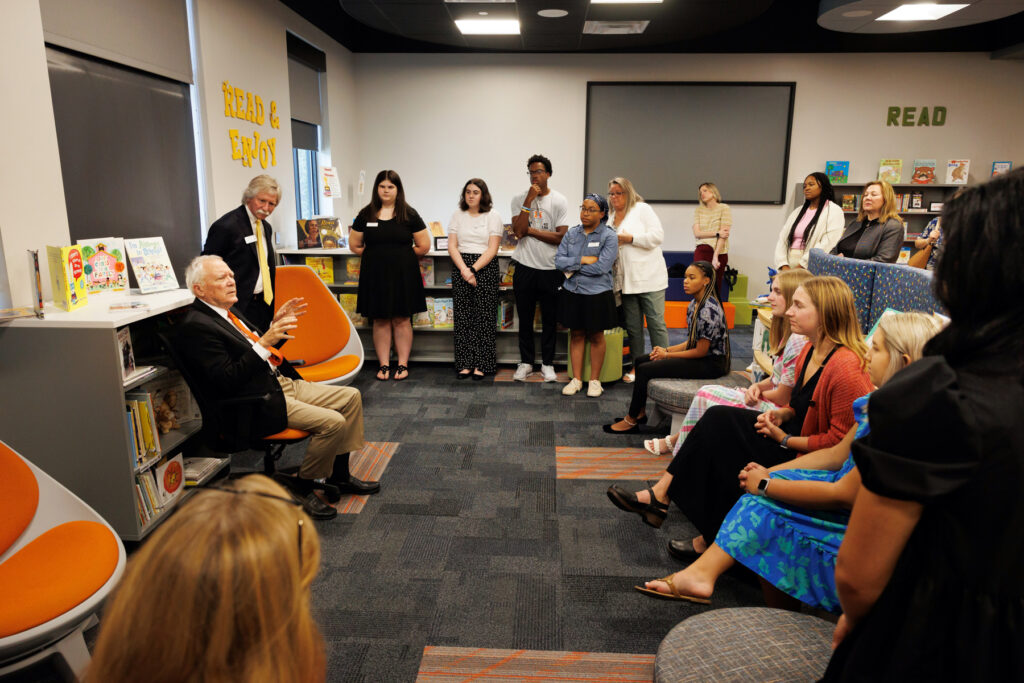 A group of people sit and stand around former Georgia Gov. Nathan Deal as he talks to them, and they listen attentively. 