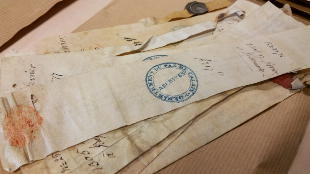 Assorted aged documents with visible handwriting and stamps, including one marked with the seal of the "National Archives." Some documents are tattered and have red wax seals.