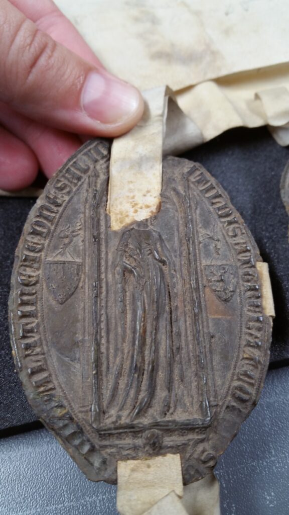 Close-up of an aged, oval-shaped medallion with ornate designs and raised lettering that reads.