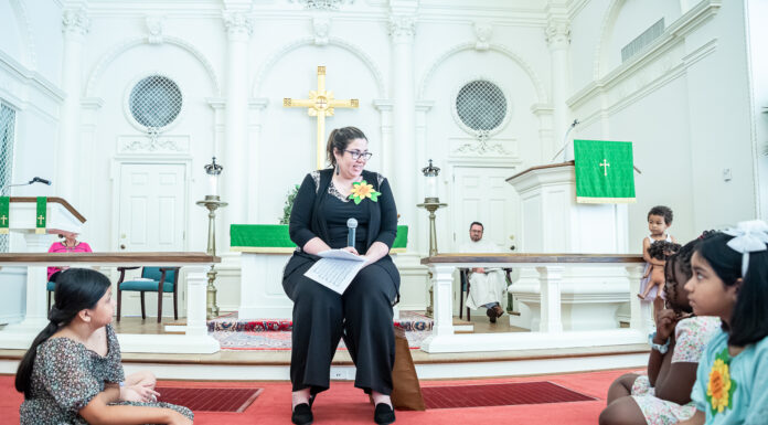 School of Theology reimagines how it supports education of church leadership Melissa Lester sits on a chair on a red carpet in the sanctuary of a church. Children sit around her.