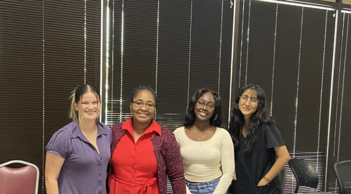 Professor’s innovative program aims to decrease teen pregnancy through storytelling Four women stand behind a table and pose for a photo, with dark blinds on the window behind them.