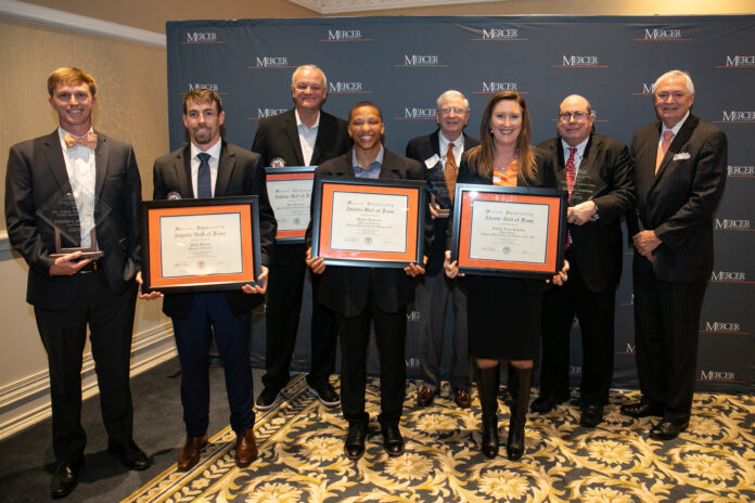 A group of eight individual stands in front of a Mercer backdrop, holding framed certificates and awards.