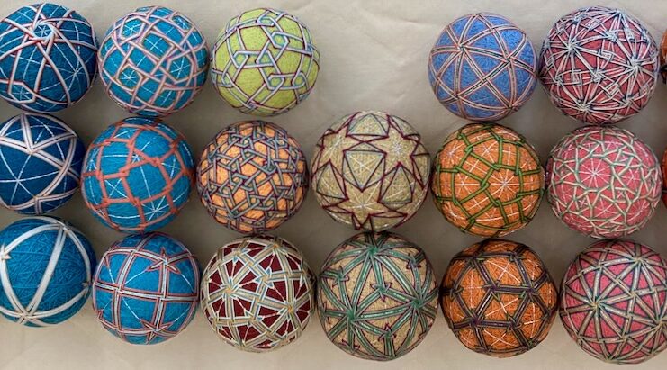 A set of colorful, intricately embroidered balls, likely handcrafted in a traditional Japanese Temari style. Each ball is adorned with geometric patterns and vibrant threadwork, showcasing a variety of designs such as stars, polygons, and intersecting lines in different color combinations.