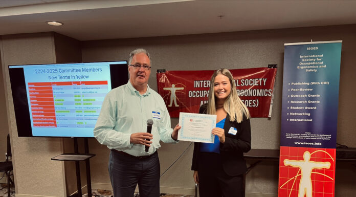 Engineering senior and alumna recognized for using virtual reality to reduce exam anxiety Two individuals at a conference, standing side by side. The man on the left is holding a microphone and smiling, while the woman on the right is holding a certificate. Behind them is a banner for the "International Society for Occupational Ergonomics and Safety" and a presentation screen showing the "2024-2025 Committee Members" list, with new members highlighted in yellow. The banner lists ISOES initiatives, including "Publishing (With DOI)," "Peer-Review," "Outreach Grants," and more. The setting appears to be indoors, in a conference room.