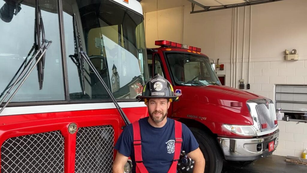 Firefighter in uniform sitting in front of a red International fire truck in a garage.