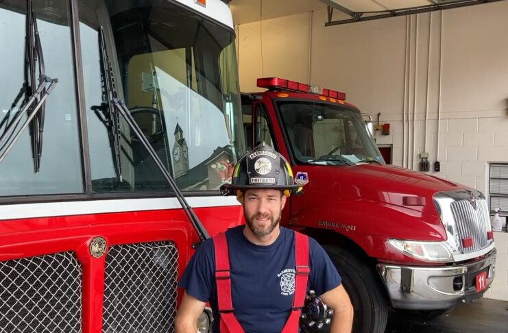 Firefighter in uniform sitting in front of a red International fire truck in a garage.