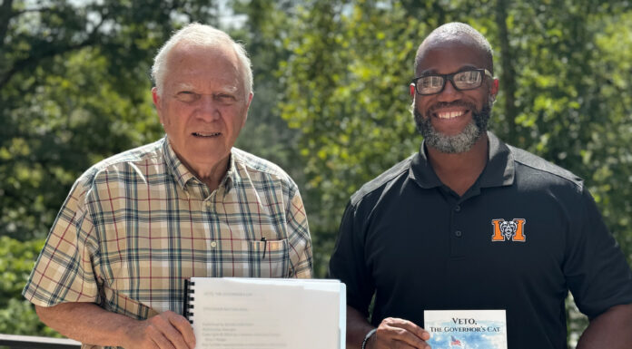 Mercer student empowers others through braille business, criminal justice work A man in a checkered button-down shirt holds a spiralbound book while a man in a Mercer University polo holds a book titled "Veto, the Governor's Cat."
