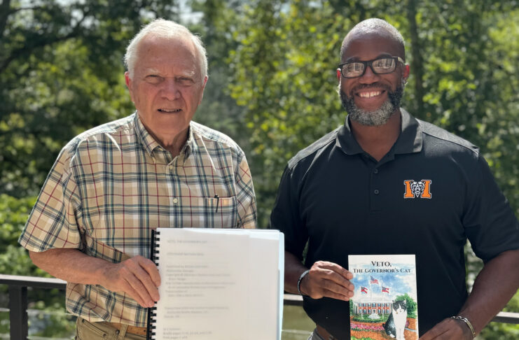 A man in a checkered button-down shirt holds a spiralbound book while a man in a Mercer University polo holds a book titled 