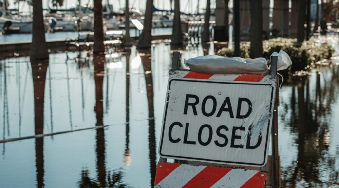 Communities come together in times of crisis but why not before? | Dr. Craig McMahan A sign that reads, "Road Closed" sits in water.