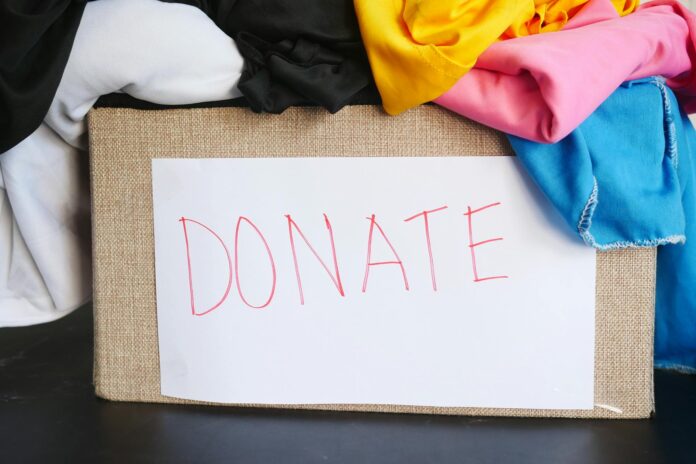 Box overflowing with colorful fabric. A white piece of paper with the word DONATE on it is taped to the box.