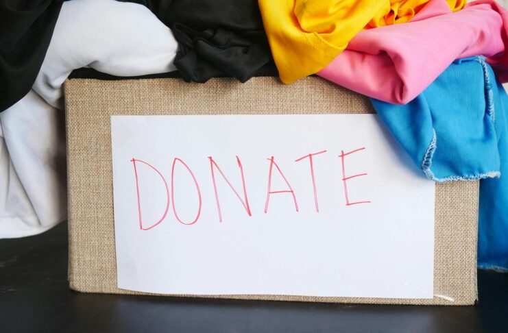 Box overflowing with colorful fabric. A white piece of paper with the word DONATE on it is taped to the box.