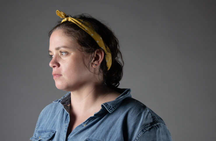 A woman in a yellow bandana and blue shirt looks off towards the left