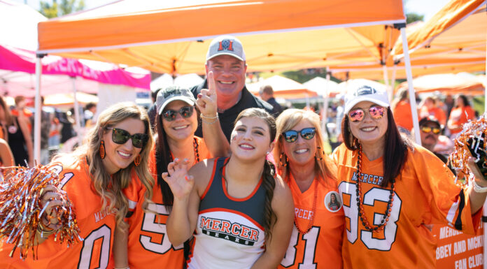 3 things to know about Mercer vs. Western Carolina football game day: Oct. 26, 2024 Group of six enthusiastic Mercer University fans wearing orange team apparel and accessories, posing together at a daytime outdoor event.