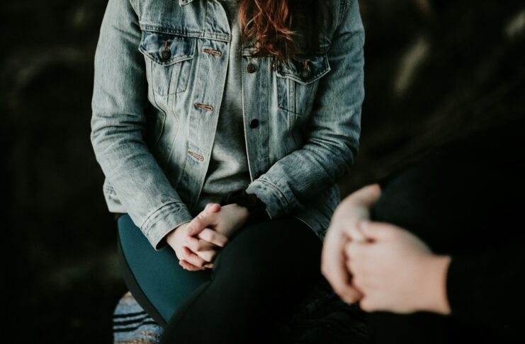 Woman wearing jean jacket with hands clasped on her lap.