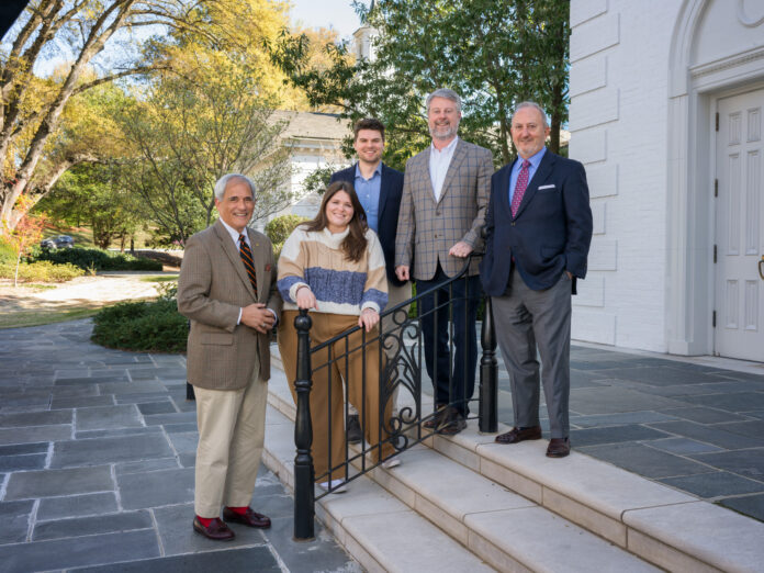 Five individuals posing together on the steps outside a church. They are professionally dressed, smiling, and standing near a black metal railing.