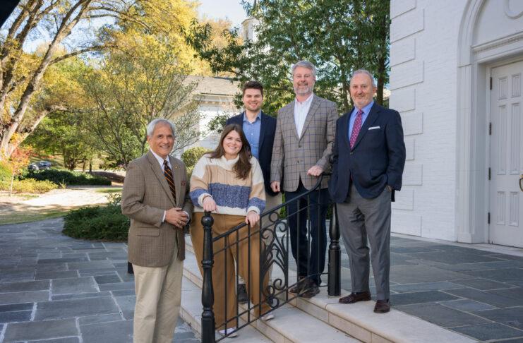 Five individuals posing together on the steps outside a church. They are professionally dressed, smiling, and standing near a black metal railing.