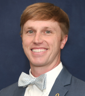 Portrait of Stephen C. Bradshaw with a bow tie, smiling, dressed in a blue blazer, with a pin on the lapel.