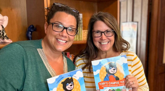Professors write, illustrate new children’s book about Mercer Two individuals smiling and holding copies of the children's book "Toby's Campus Tour" inside a room.