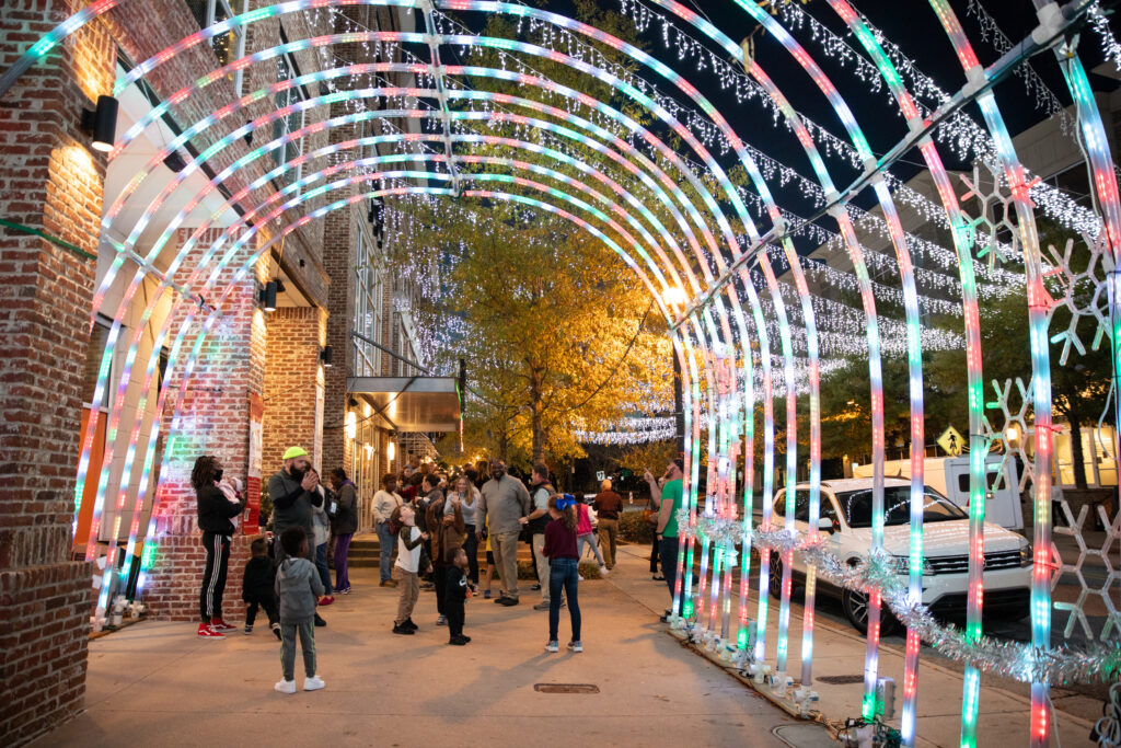 People walk through a brightly lit tunnel at night, with festive lights and decorations on a city street.
