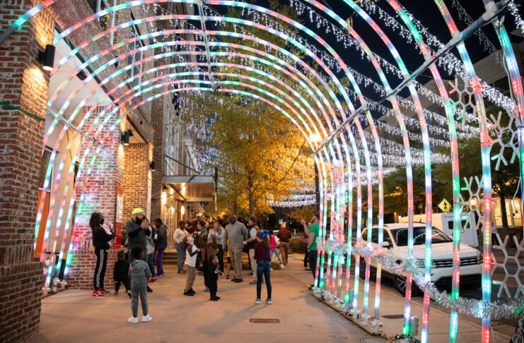 People walk through a brightly lit tunnel at night, with festive lights and decorations on a city street.