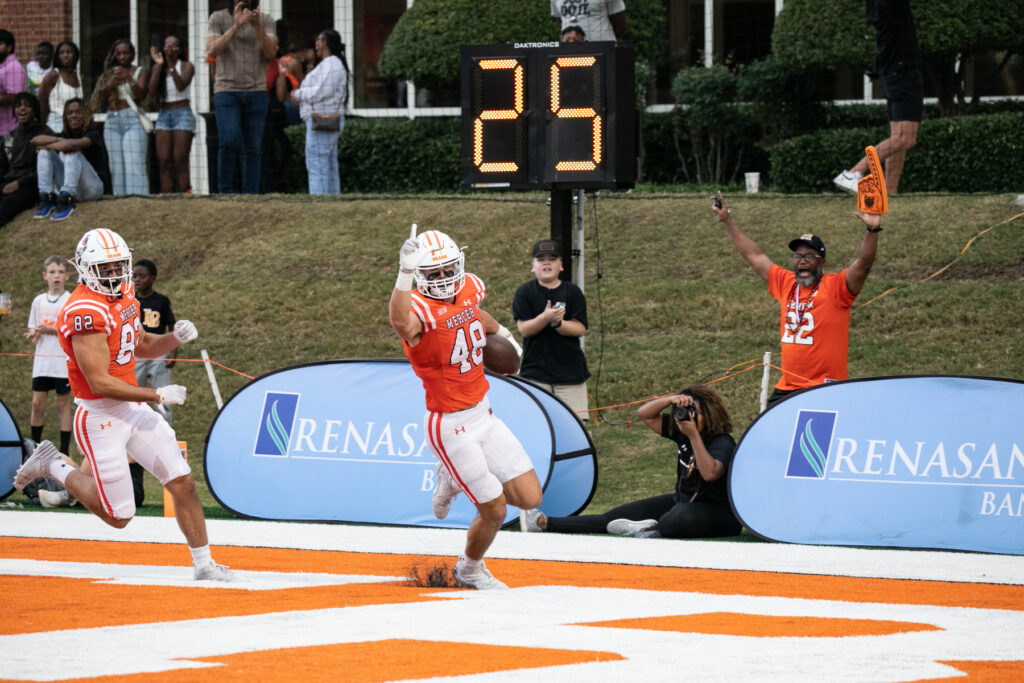 A Mercer football player celebrates a touchdown in the end zone as spectators cheer.