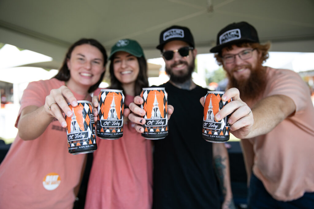 Four people holding out cans of Ole Toby craft beer.