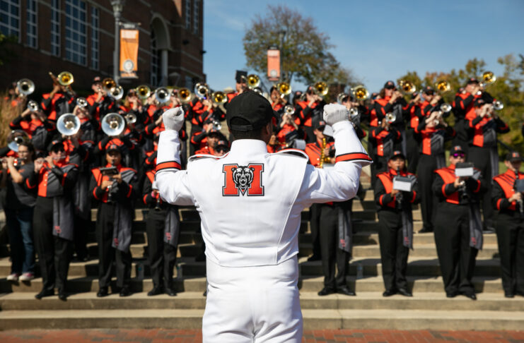 A drum major leads the Mercer marching band during a performance on outdoor steps.