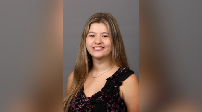 Junior selected for $5,000 Women in Transportation scholarship A young woman with long hair smiles at the camera, wearing a floral dress with ruffles, set against a gray background.