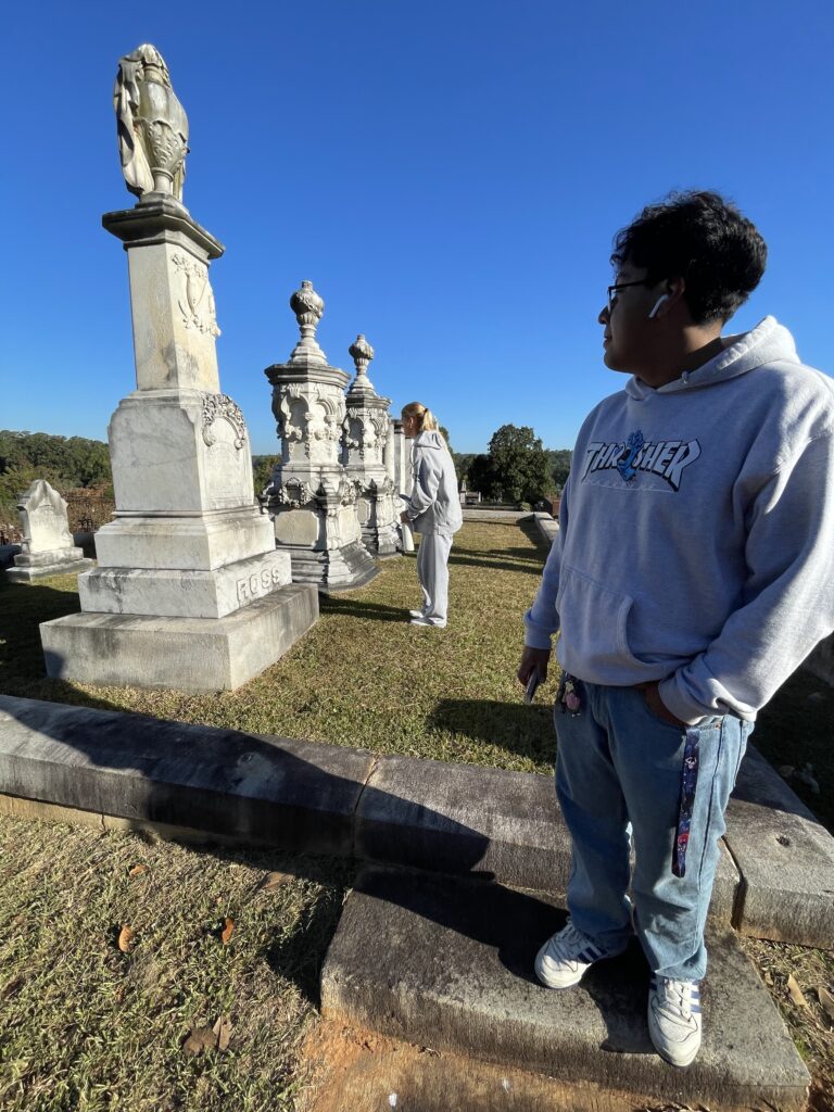 Man looks left towards elaborate cemetery headstones.