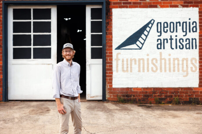 Andrew Eck standing in front of a brick building with a sign reading Georgia Artisan Furnishings.