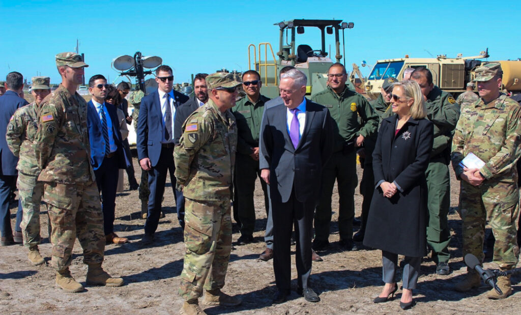 Craig Mattoon talks to James Mattis and Kirstjen Nielsen outdoors, with a group of people standing around them.