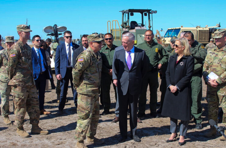 Craig Mattoon talks to James Mattis and Kirstjen Nielsen outdoors, with a group of people standing around them.