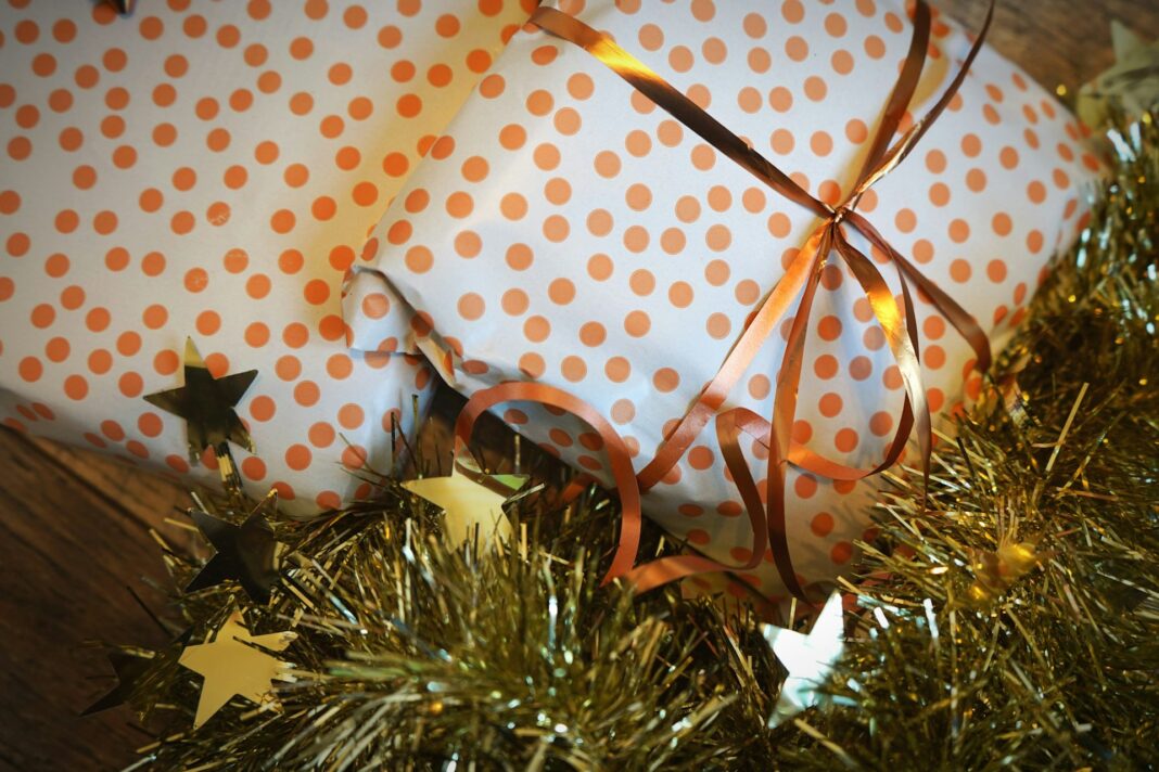 Two gifts wrapped in orange polka dot paper with an orange ribbon, surrounded by gold tinsel and star decorations.