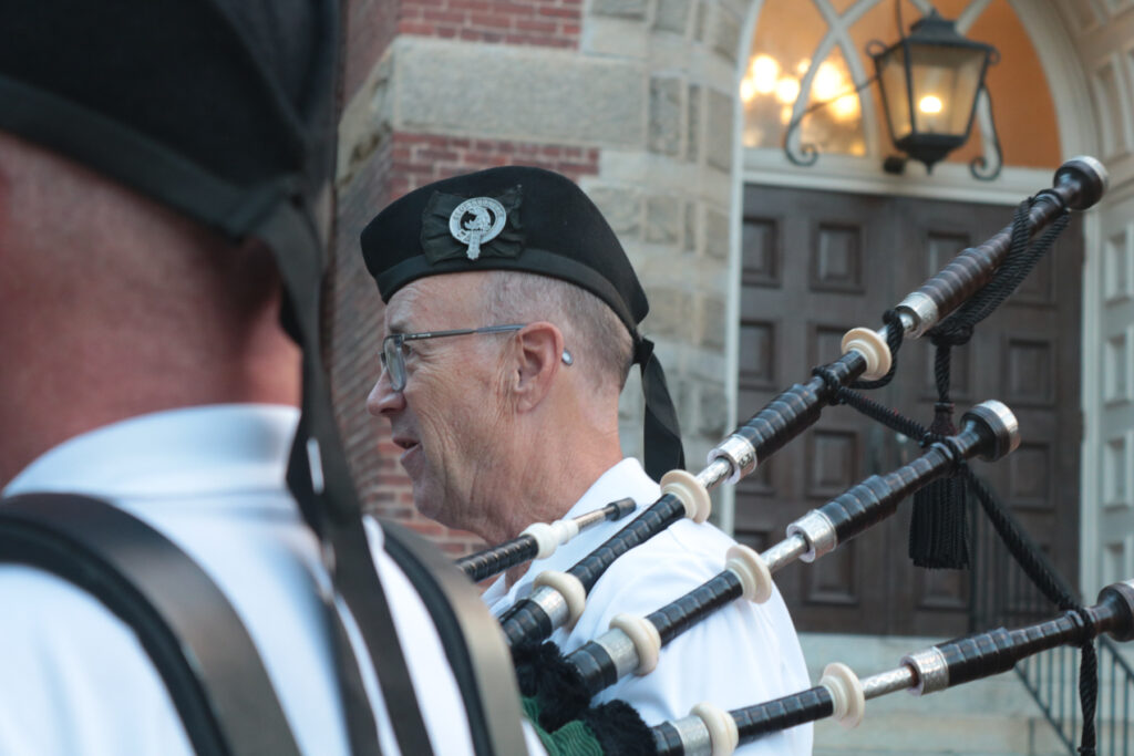 Person in traditional Scottish attire playing with the bagpipes over his shoulder.