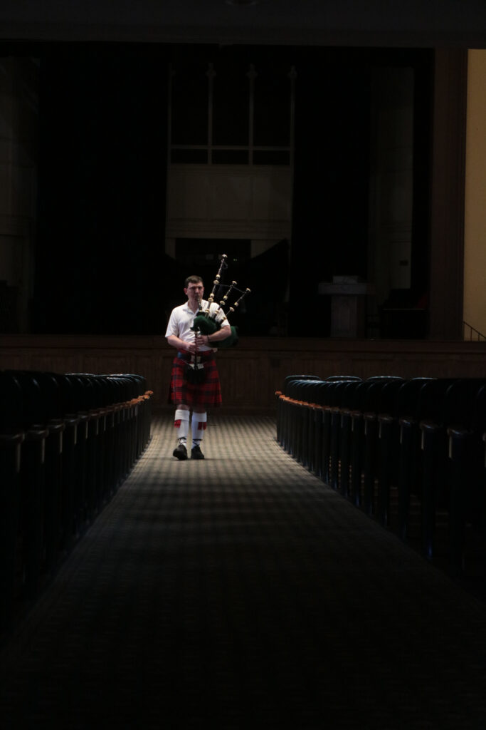 Individual in a kilt playing bagpipes inside a dimly lit aisle.