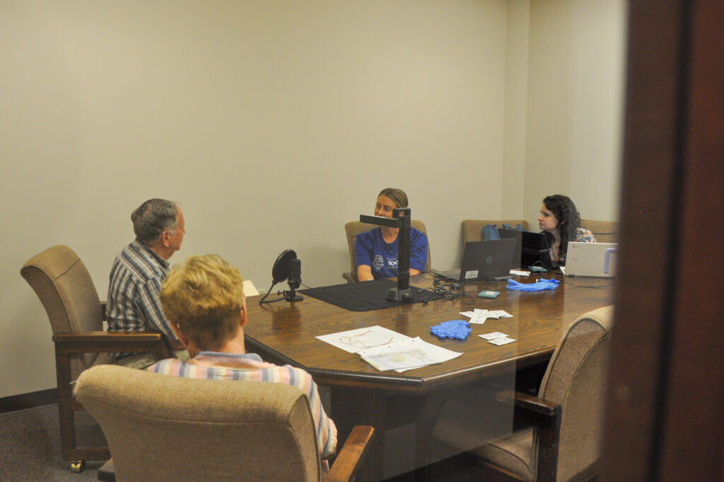 Four individuals in a meeting room. The setting suggests a professional or office environment.